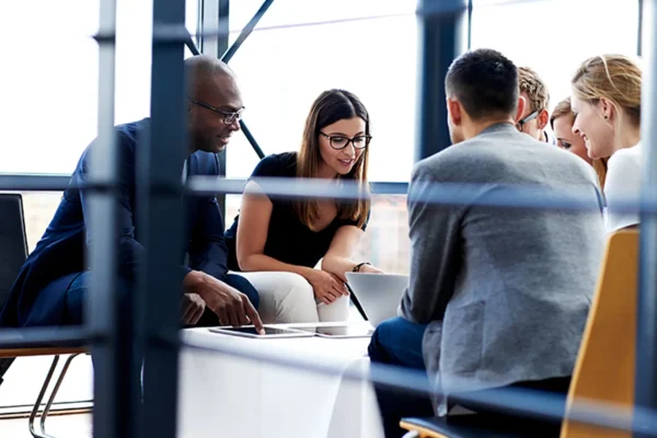 Five people sit around a table in an office, looking at documents and a laptop, engaged in a discussion.