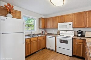 Kitchen with wooden cabinets, white appliances including a refrigerator, stove, microwave, and dishwasher, and a window above a double sink.