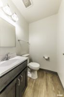 Small bathroom with a dark wood vanity, sink, mirror, toilet, towel bar, toilet paper holder, and light wood floor.