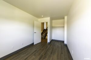 Empty room with white walls, open door revealing stairs, wood-style flooring, and an open closet with a shelf and hanging rod.