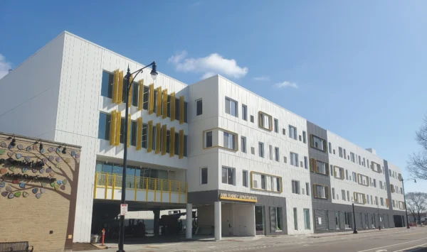 Modern three-story building with white exterior, yellow accents, and numerous windows, labeled "Ann Arbor Art Center," situated on a clear, sunny day.
