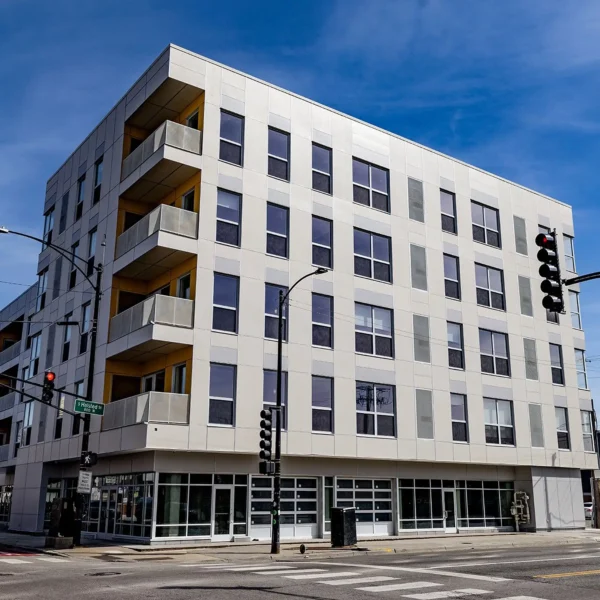 A modern five-story apartment building with large windows and balconies on a street corner, viewed during the daytime.