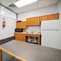 Small office kitchen with wooden cabinets, a white fridge, a microwave, a sink, countertop, and a fire extinguisher mounted on the wall.