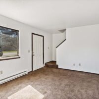 Unfurnished room with brown carpet, white walls, a window, front door, and a small staircase leading up.