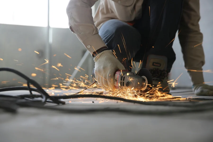 A person wearing gloves uses an angle grinder, producing sparks while working on the floor.
