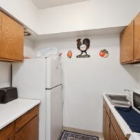 Small kitchen with white appliances, wooden cabinets, a black toaster, a microwave, and rooster-themed wall decor above the refrigerator.