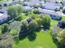 Aerial view of residential apartment buildings surrounded by green lawns, mature trees, and a winding walking path.