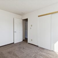 Empty room with white walls, brown carpet, a white door partially open, and a white sliding closet door.