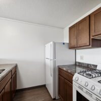 Small kitchen with brown cabinets, a white refrigerator, a gas stove, marble-patterned countertops, and a stainless steel sink.