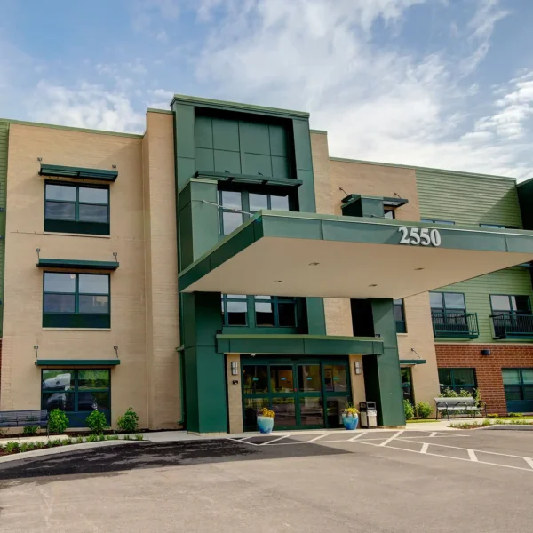 Modern three-story building with beige and green exterior, large entrance canopy displaying the number 2550, and accessible parking spaces in front.