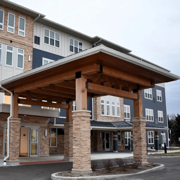 A modern three-story building with a wood and stone entrance canopy, large windows, and a circular driveway in front.