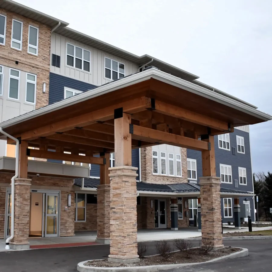 A modern three-story building with a wood and stone entrance canopy, large windows, and a circular driveway in front.