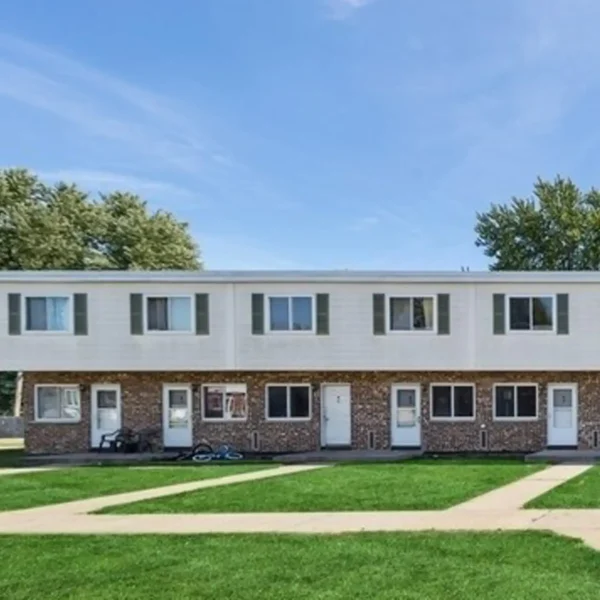 A two-story brick apartment building with five white doors, several windows, and a grassy lawn with sidewalks in front.