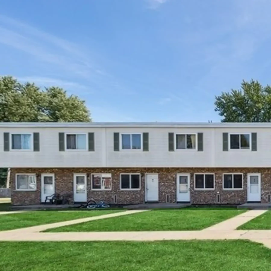 A two-story brick apartment building with five white doors, several windows, and a grassy lawn with sidewalks in front.