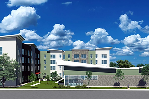 Modern multi-story apartment building with green and beige exterior, large windows, and a separate community center, set against a partly cloudy sky.