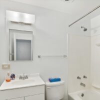 A white bathroom with a sink, mirror, toilet, and bathtub-shower combination; toiletries and tissue box are on the sink and toilet.