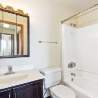 Small bathroom with a white bathtub and shower, toilet, dark vanity with sink, mirrored cabinet, and overhead lights.