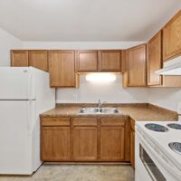 Small kitchen with wooden cabinets, a white refrigerator, electric stove, double sink, under-cabinet light, and brown countertops.