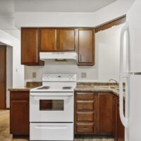 A small kitchen with brown cabinets, a white stove and range hood, granite-style countertops, and a white refrigerator.
