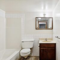 A small bathroom with a bathtub and shower, toilet, wooden vanity with a sink, wall mirror, tile backsplash, and overhead light.