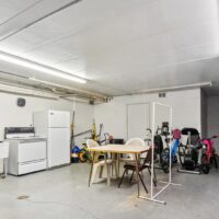 A garage with a table and chairs in the center, surrounded by a stove, refrigerator, bicycles, cleaning tools, and miscellaneous household items.