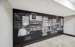 A black-and-white mural on a hallway wall features vintage photos, architectural drawings, and documents related to Winton Manor and local hotel history.