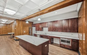 Modern kitchen with dark wood cabinets, white countertops, an island, built-in microwave, and wood-paneled walls, under recessed and pendant lighting.