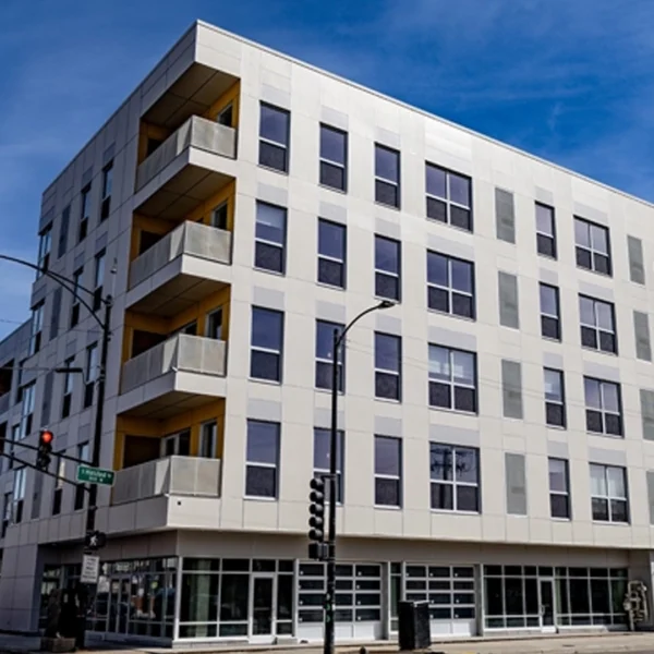 A modern four-story apartment building with square windows, balconies, and ground-floor retail space on a city street corner.