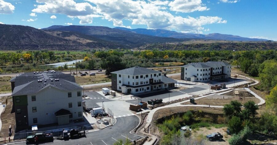 Aerial view of a residential housing complex under construction, surrounded by natural landscape, mountains, and a river in the background.