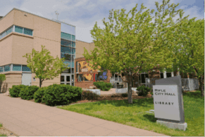 Modern building with large windows and trees in front, sign in foreground reads "Rifle City Hall Library.
