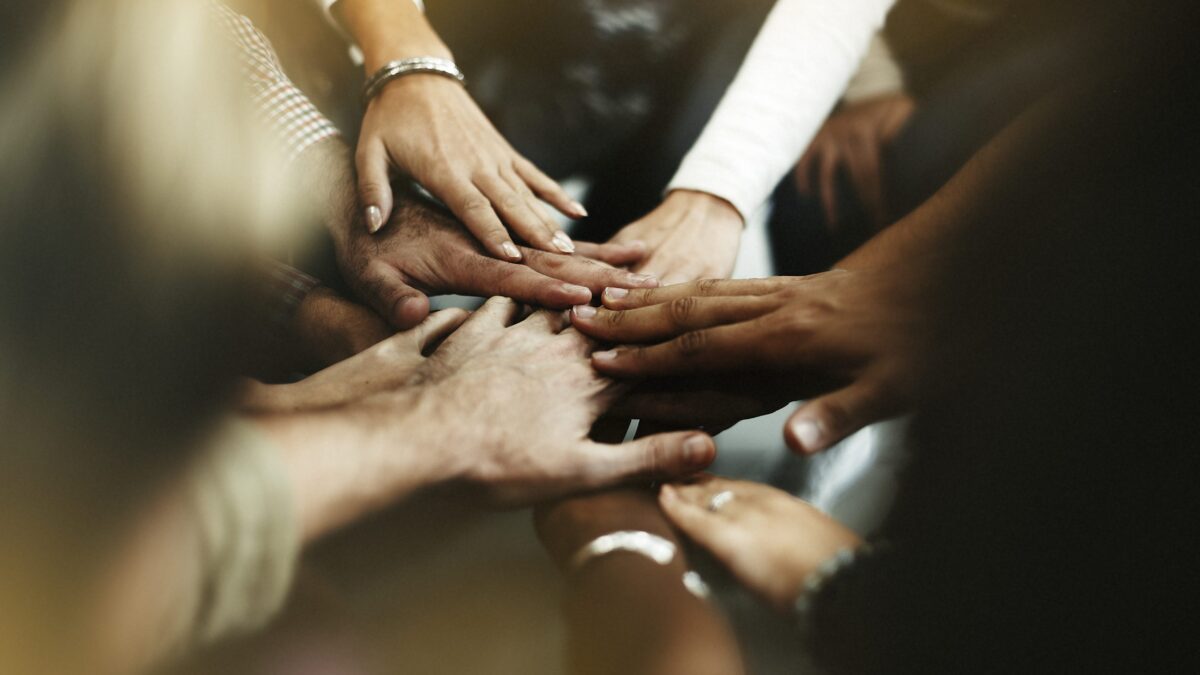 A group of people place their hands together in the center, showing unity and teamwork.