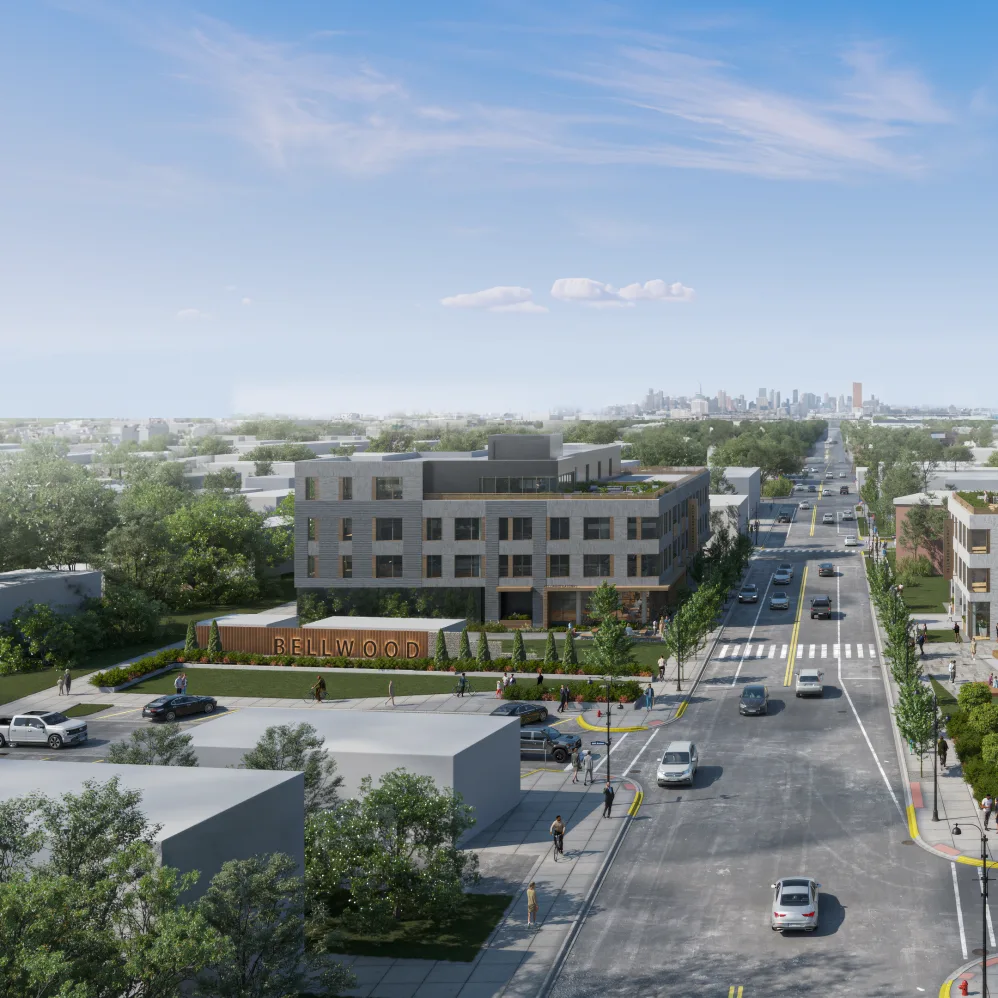 Aerial view of a modern three-story building labeled "BELLWOOD" at a street intersection, with cars, trees, and people visible, city skyline in the distance.