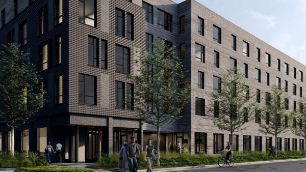 A modern five-story apartment building with dark brick exterior, large windows, trees along the sidewalk, and several people walking and cycling nearby.