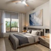 Modern bedroom with a large bed, two nightstands with lamps, a ceiling fan, abstract wall art, and a window with curtains overlooking greenery.
