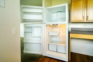 An empty white refrigerator with both the fridge and freezer doors open, showing clean shelves and drawers in a kitchen setting.