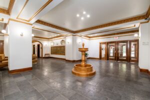 A lobby with a stone-tiled floor, a central stone fountain, and a wall of mailboxes.