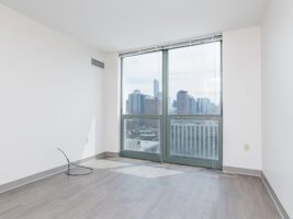 Empty room with wood-look flooring, white walls, and a large window overlooking a city skyline.