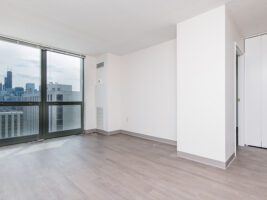 Empty room with gray wood-look flooring, white walls, and floor-to-ceiling windows overlooking a city skyline.