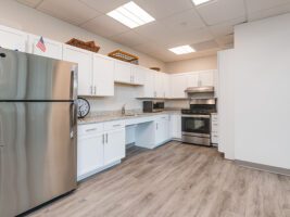 A kitchen with white cabinets, granite countertops, a stainless steel refrigerator, and a gas range.