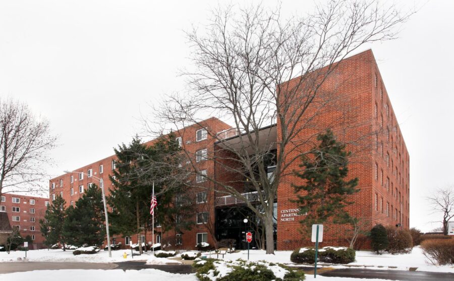 A red brick apartment building named Centennial Apartments North with a snow-covered parking lot in front.