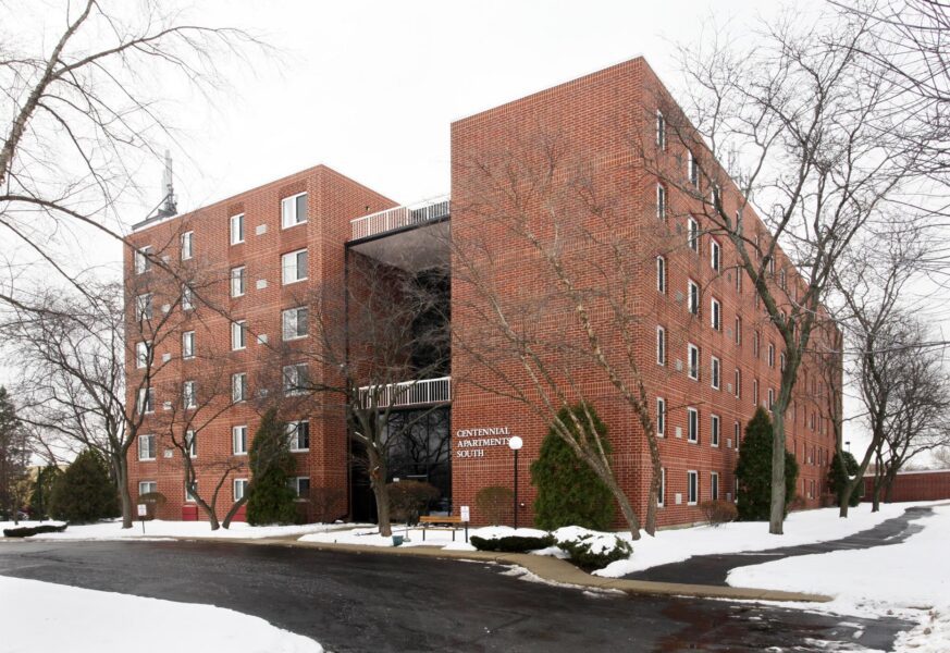 Centennial Apartments South, a multi-story red brick apartment building surrounded by bare trees and light snow.