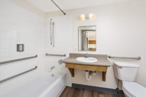 Accessible bathroom with a white bathtub, grab bars, a wall-mounted vanity with a sink, and a toilet.