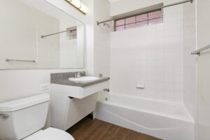 Bathroom with a white toilet, vanity with a speckled countertop and sink, and a tiled shower-tub combination.