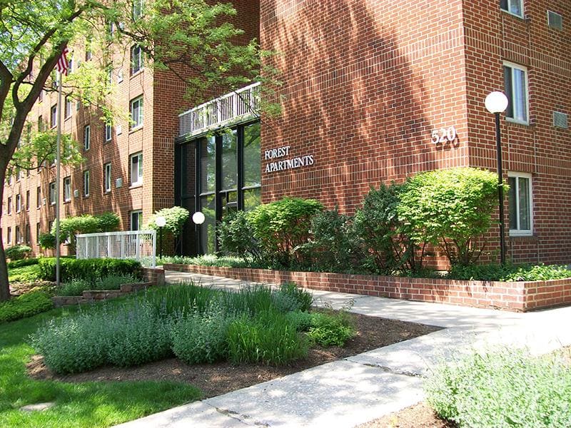 A brick apartment building with a sign that reads “Forest Apartments” and the address “520” above the entrance.