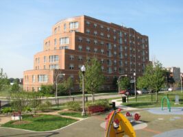 A multi-story red brick apartment building with balconies, seen from a playground with colorful play equipment.