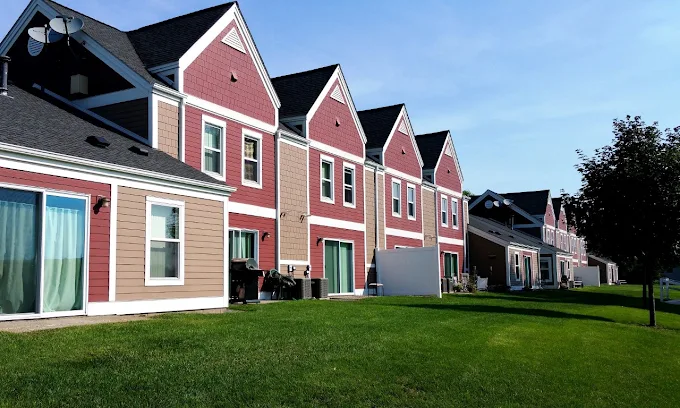 A row of multi-story townhouses with red and beige siding, seen from a lawn.