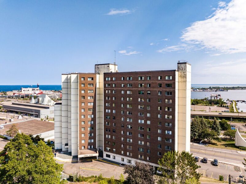 Aerial view of the multi-story brown brick Ledge Place apartment building situated near a waterfront.