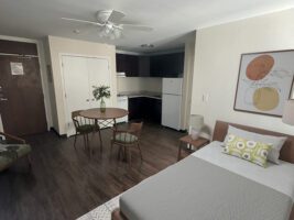 A studio apartment with a bed, a dining table for two, and a small kitchen with a refrigerator and stove.
