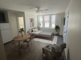 Studio apartment with a bed, dining table, armchair, and kitchenette.