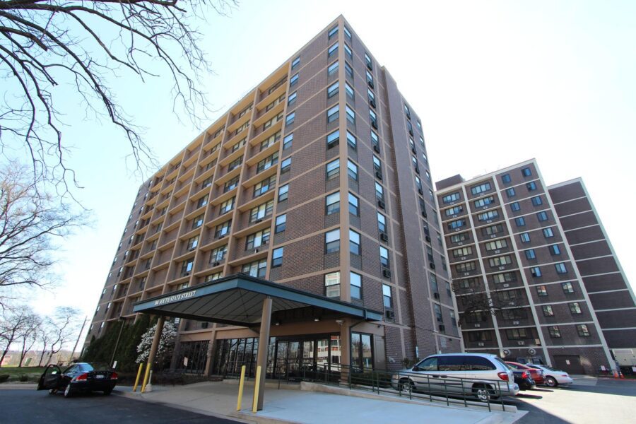 Low-angle view of a large, brown brick apartment building with a covered entrance marked “104 South State Street.”